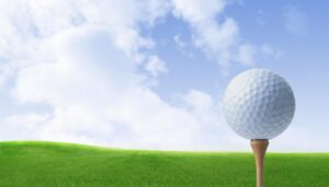 Golf ball on a tee on a green fairway with a blue sky and clouds in the background.